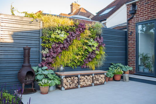 A photo of a garden decking area on a sunny day. With a living wall of plants, a wood pile an outdoor chimenea 