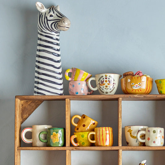 Wooden shelf unit with various mugs displayed. With a tall whimsical zebra head statue on the left.