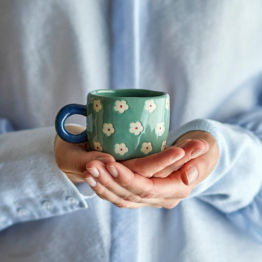 Person holding a blue mug with floral patterns against a blurred background