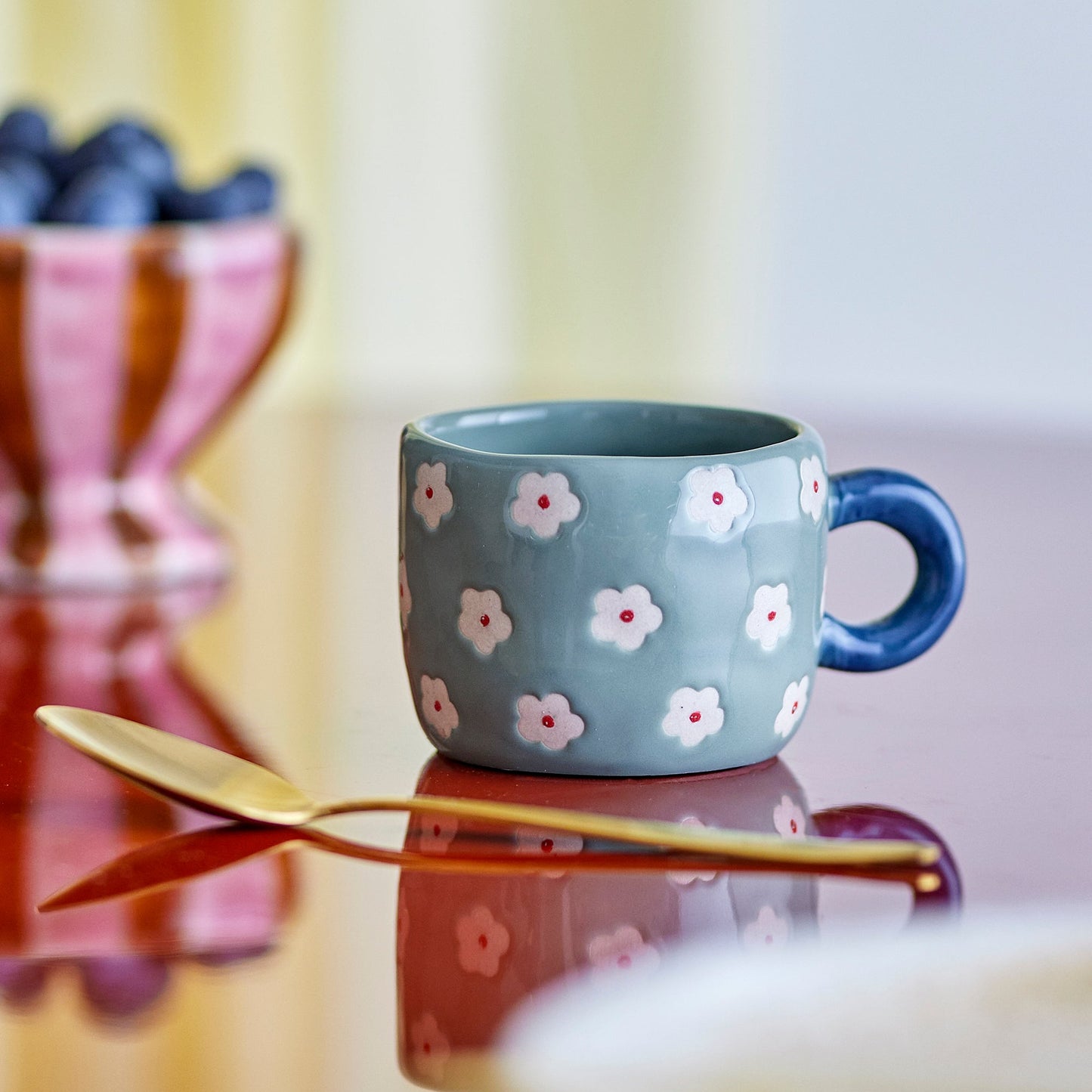 Blue mug with floral pattern on a reflective surface with a blurred background