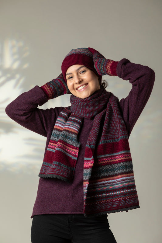 Person wearing a maroon outfit with a patterned scarf and hat against a neutral background