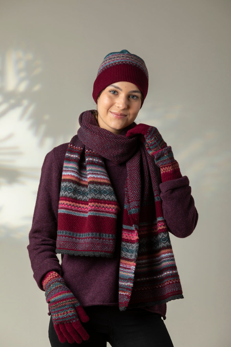 Person wearing a patterned scarf, hat, and gloves against a neutral background