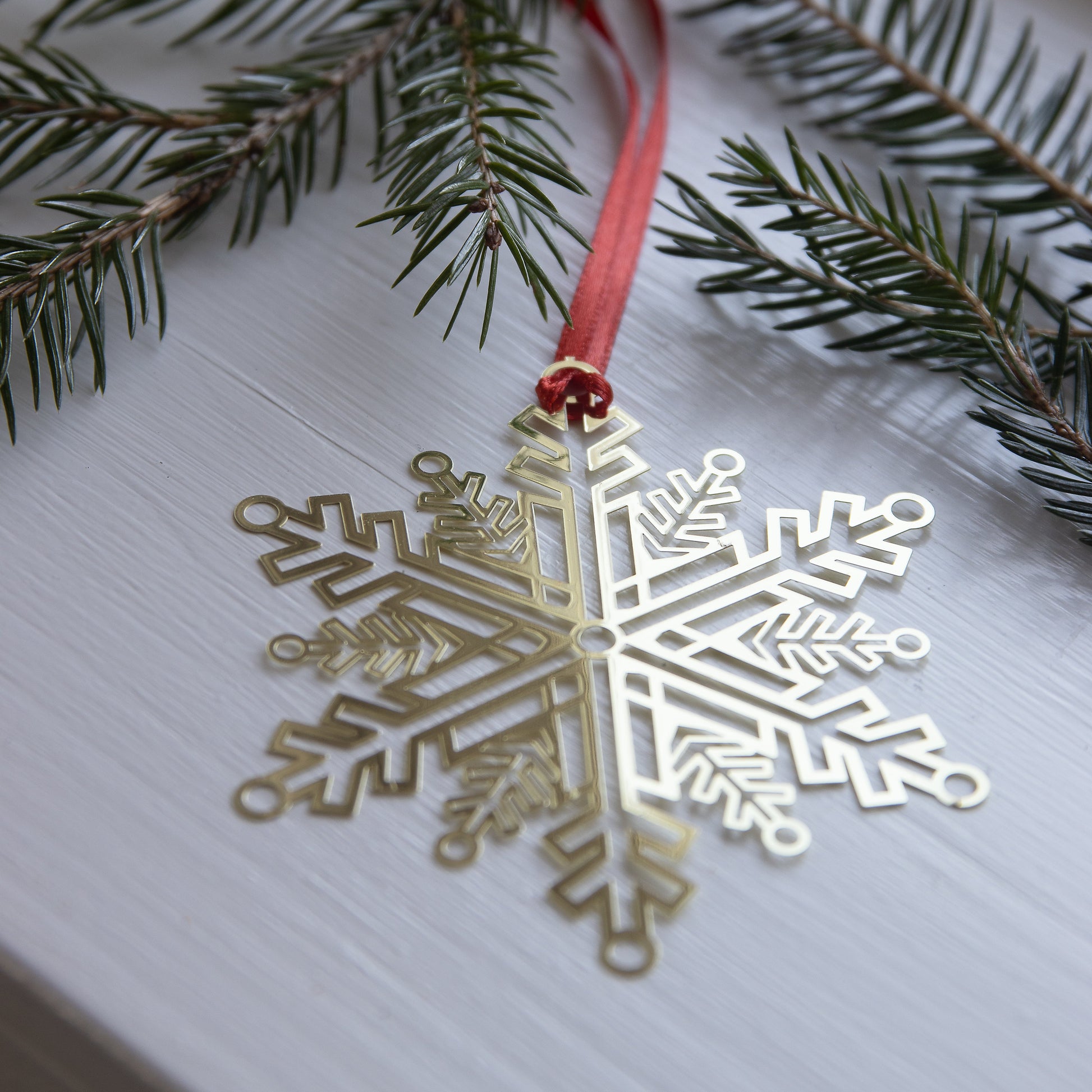 Gold snowflake ornament on a white surface with green branches and a red ribbon.