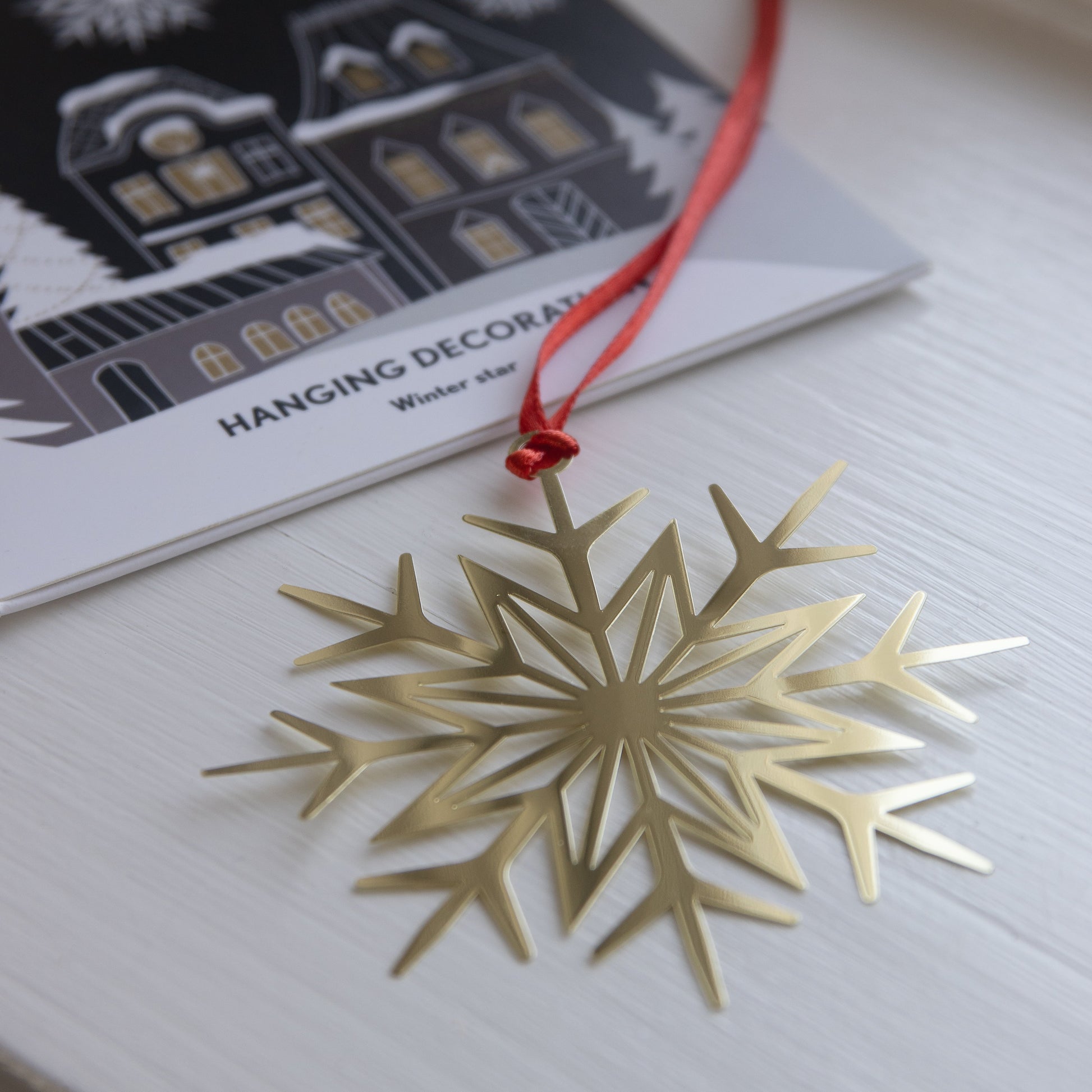 Gold snowflake ornament with a red string on a white surface