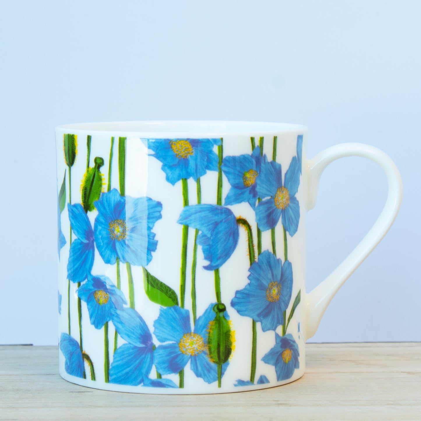 A white ceramic mug with a floral pattern featuring blue flowers and green leaves on a wooden surface.