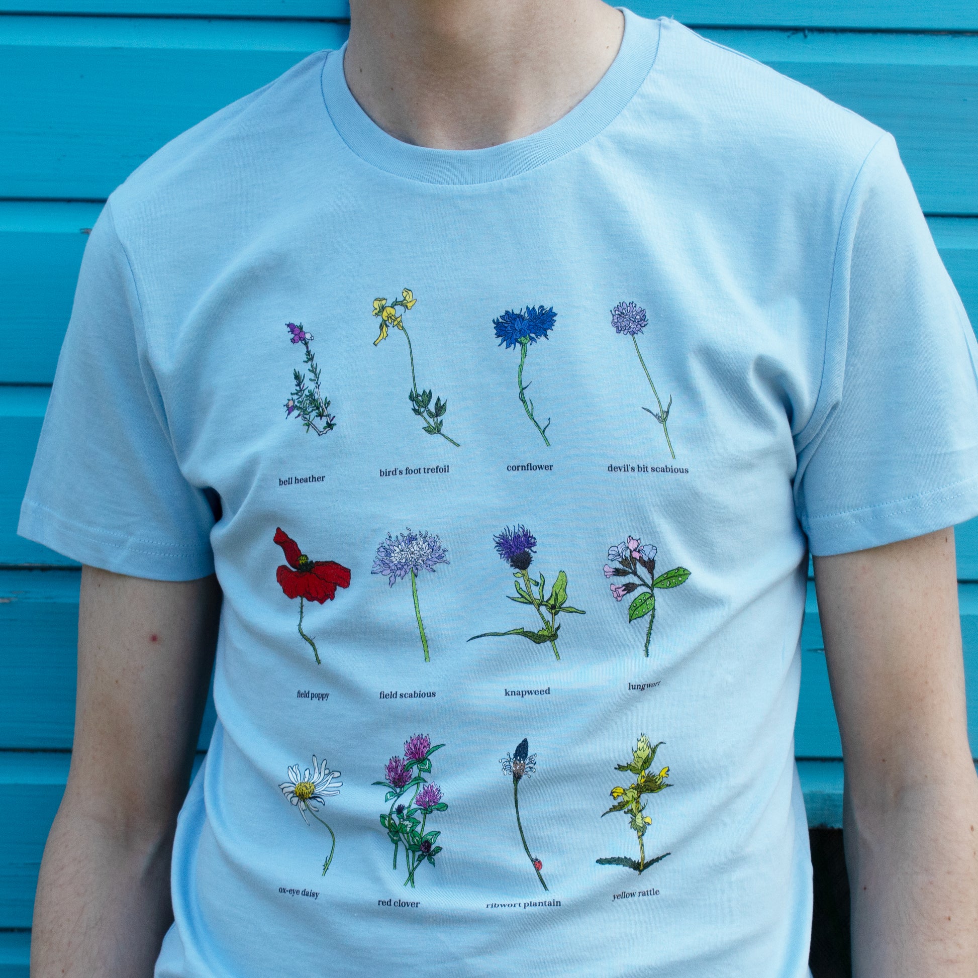 Light blue t-shirt with embroidered floral designs against a blue wooden background