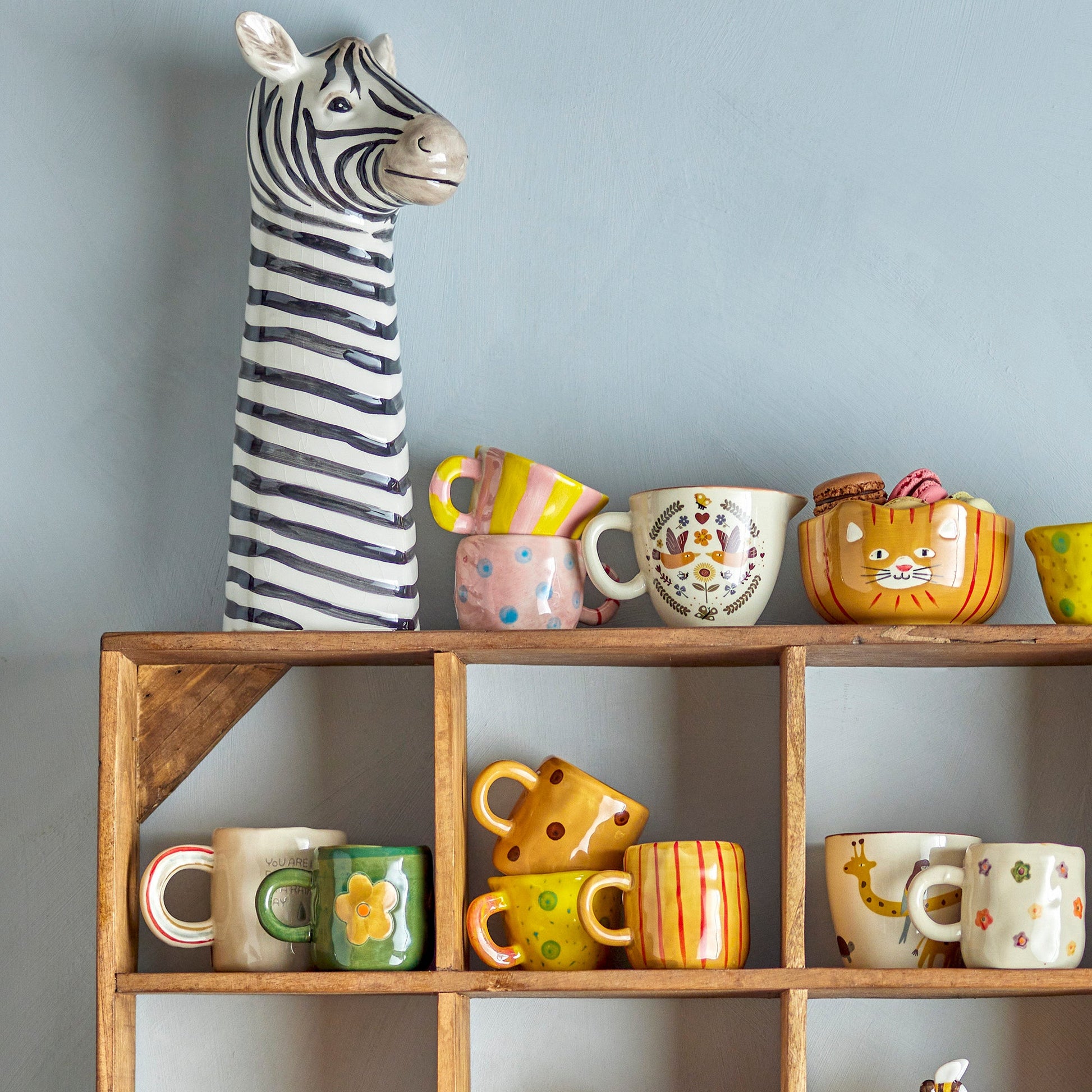 Wooden shelf unit with various mugs displayed. With a tall whimsical zebra head statue on the left. 