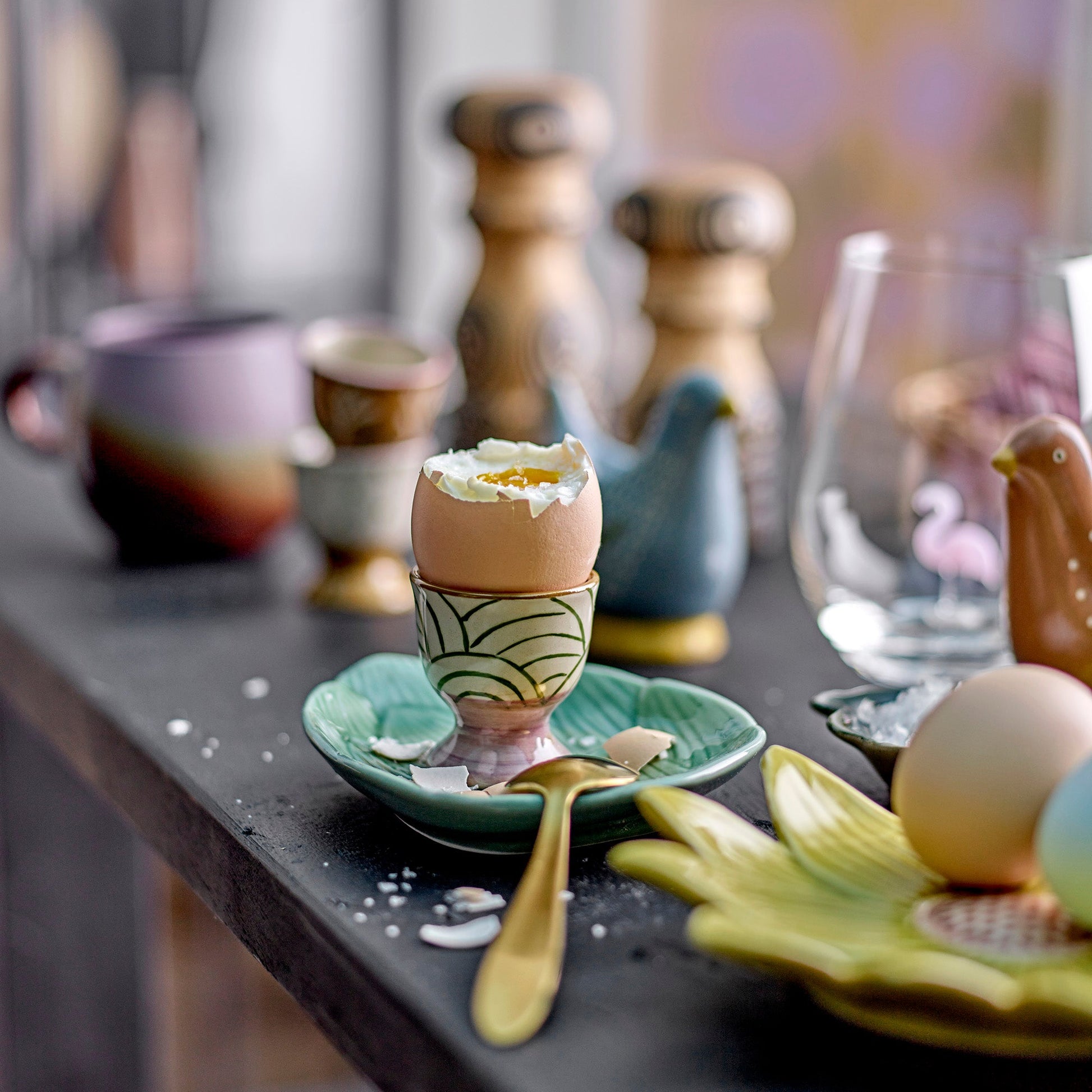 Green Stripe egg cup with egg on a busy tablescape. 