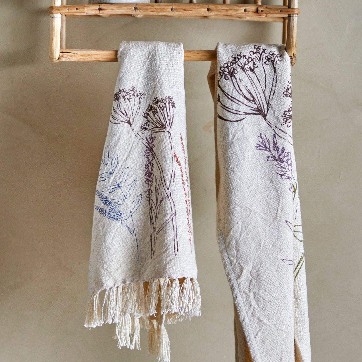 two tea towels with sketched flowers design hanging on a wooden towel rail. 