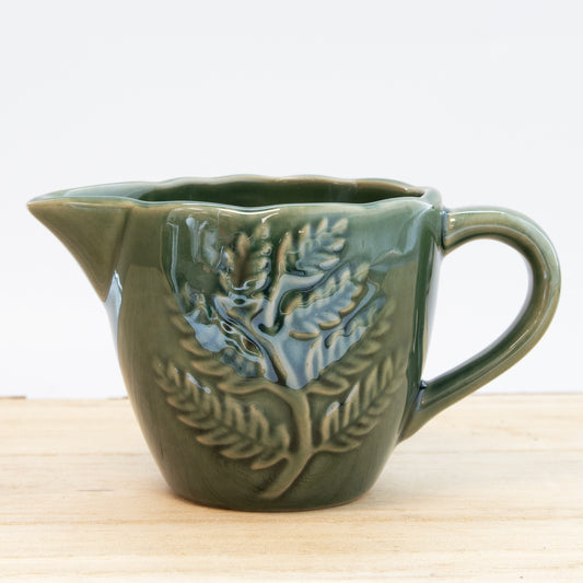 Green ceramic pitcher with leaf design on a wooden surface