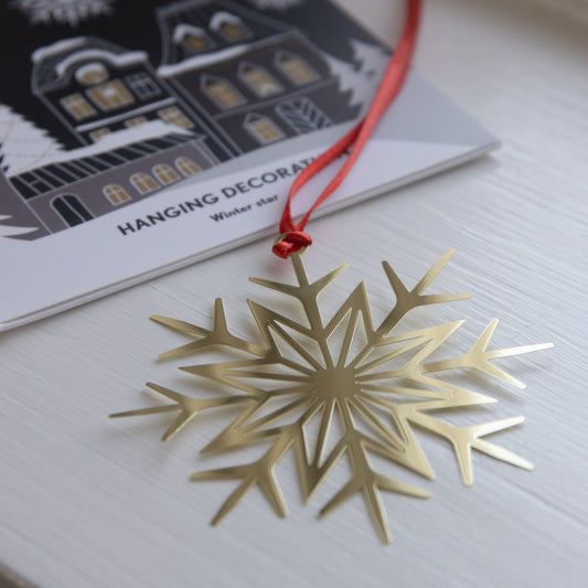 Gold snowflake ornament with a red string on a white surface