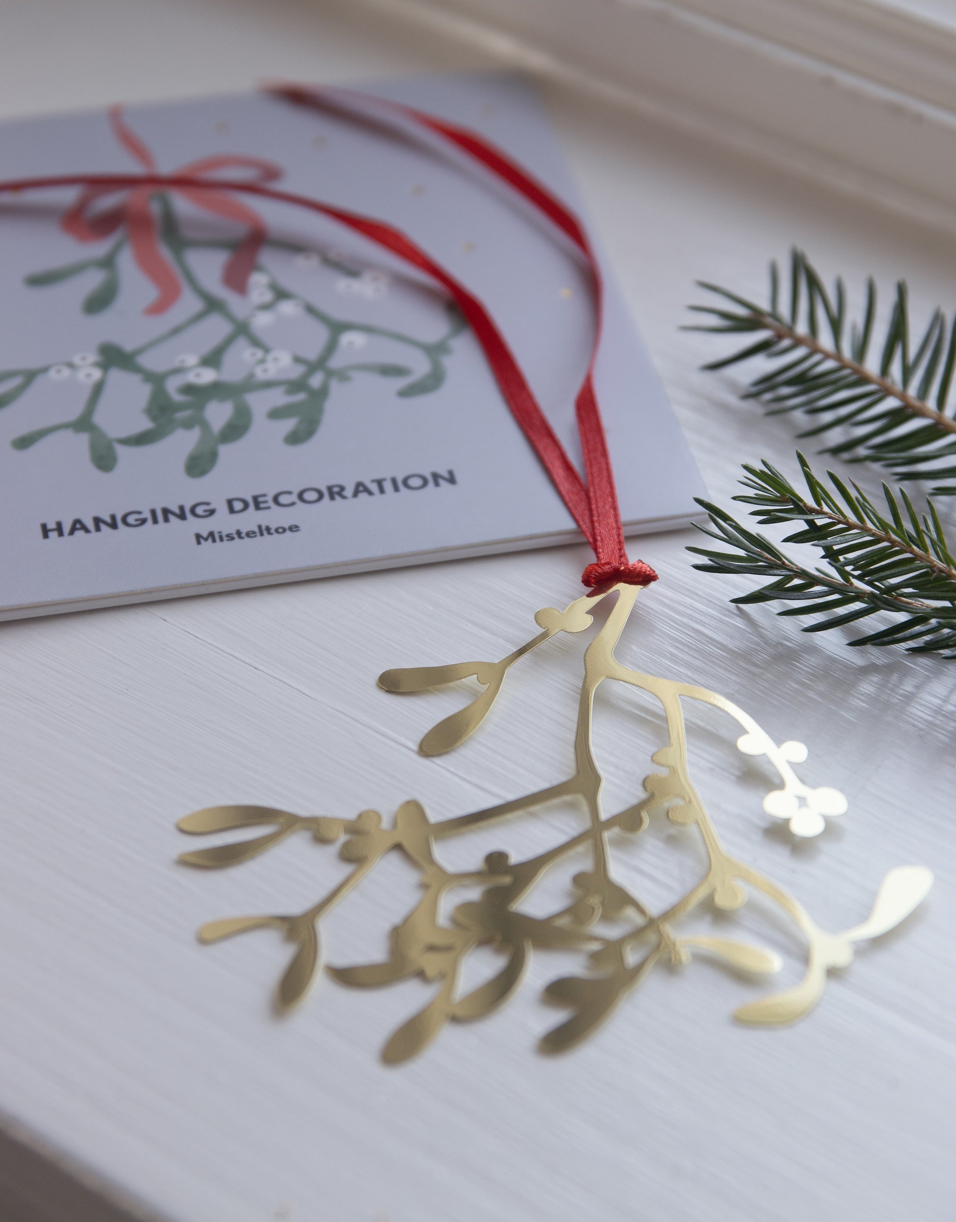 Gold mistletoe decoration on a white surface with a card in the background