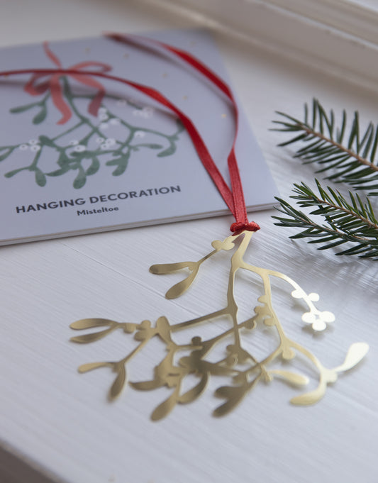 Gold mistletoe decoration on a white surface with a card in the background